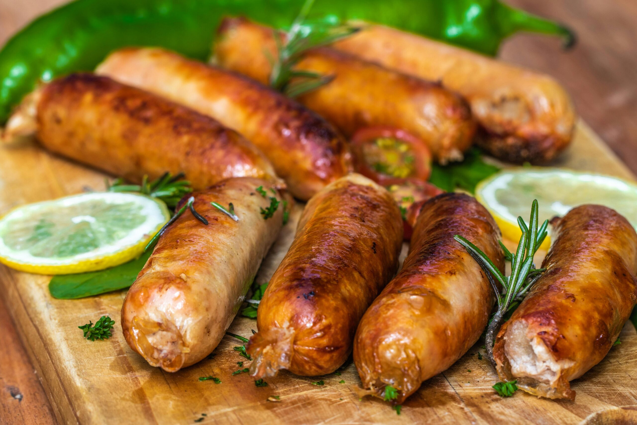 Juicy grilled sausages on a wooden board with lemon slices and herbs.